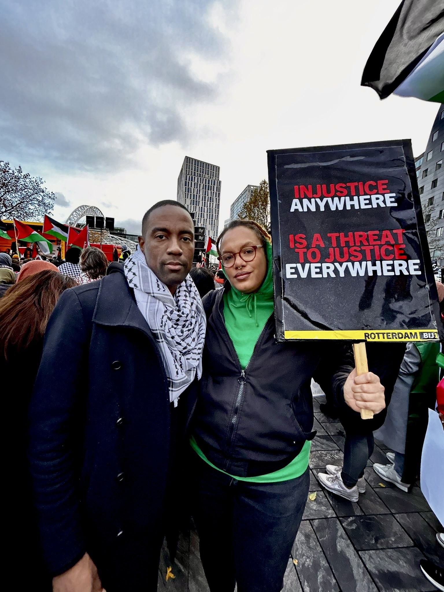 Foto tijdens de demonstratie met Edson Olf en Lisa Mc Cray. Lisa heeft een bord vast van Rotterdam BIJ1 met de tekst: 'INJUSTICE ANYWHERE, IS A THREAT TO JUSTICE EVERYWHERE'.